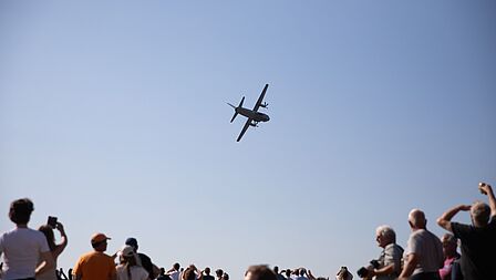 Publiek kijkt naar een overvliegend militair vliegtuig.